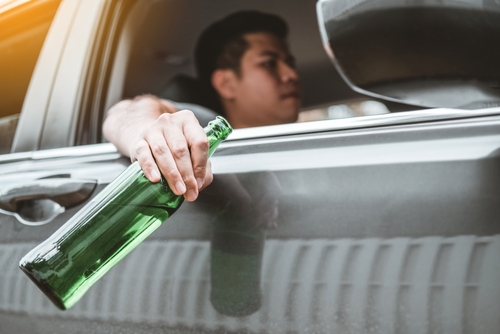 Driver holding a green beer bottle out of a car window, representing drunk or impaired driving behavior.
