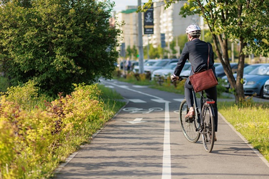 Stylish business man in helmet and suit cycling on bike path in sunny day. Back view of male employee with brown leather briefcase riding on bicycle in town. Concept of eco transport.